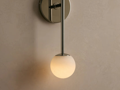 Wall-mounted light fixture with chrome finish and two frosted glass globes, vertically aligned on a beige wall next to a round mirror edge.