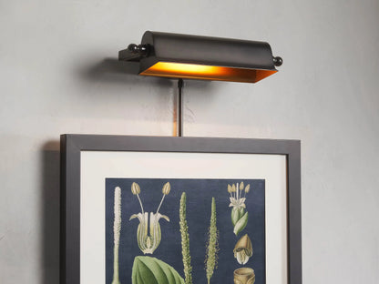 Tremont Bronze Library Sconce mounted above framed botanical artwork, emitting warm light onto the image below.