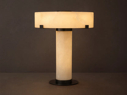 Chayla Table Lamp with cylindrical alabaster base, wide circular alabaster shade, and dark brass accents on a wooden surface.