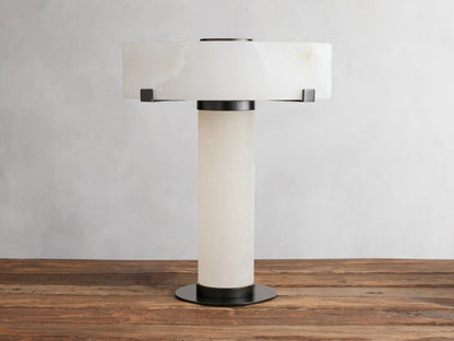 Chayla Table Lamp with cylindrical alabaster base, wide circular alabaster shade, and dark brass accents on a wooden surface.