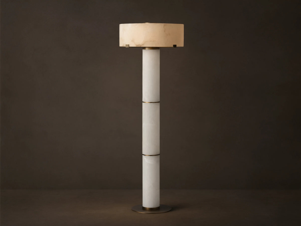 Chayla Floor Lamp: Tall, segmented white alabaster column, glowing cylindrical shade with natural patterns, antique brass accents, wood floor.