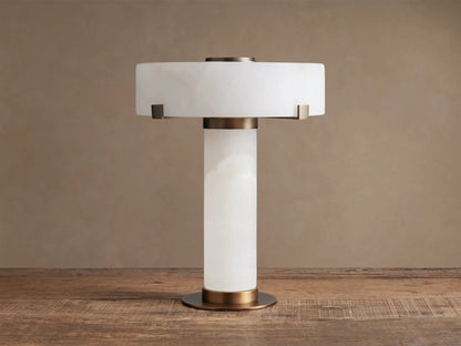 Chayla Table Lamp: white alabaster cylindrical body, drum shade, antique brass accents, on wooden table.