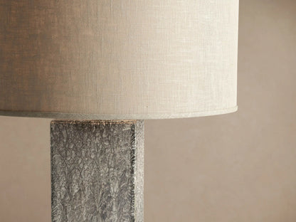 Adrano Table Lamp featuring a rectangular, textured fused silver cast glass base and a natural linen drum shade on wood.