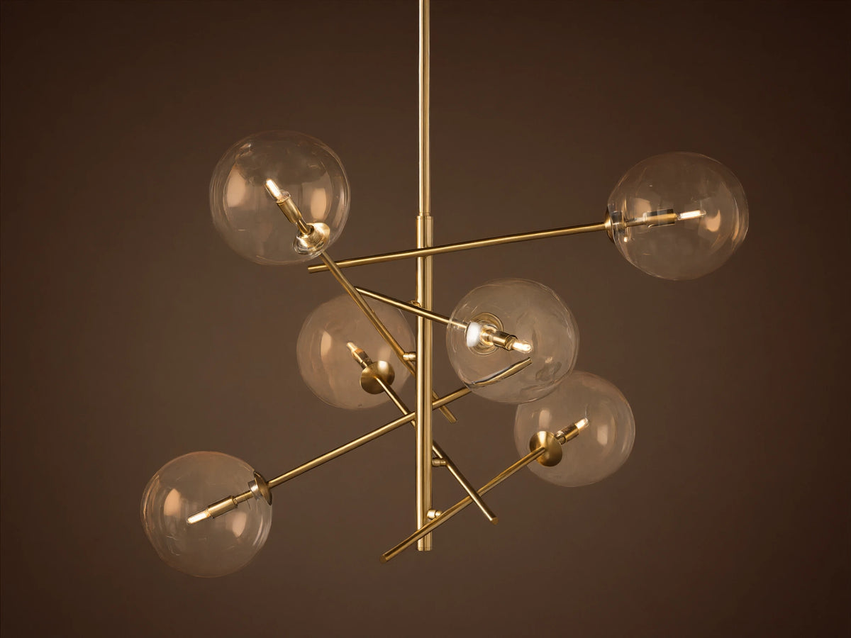 Roscoe Chandelier featuring a brass frame with six clear glass globes extending from a central pole, against a plain wall.