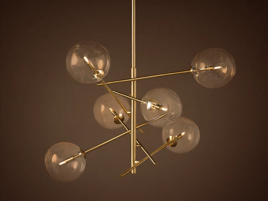Roscoe Chandelier featuring a brass frame with six clear glass globes extending from a central pole, against a plain wall.