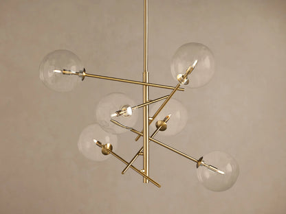 Roscoe Chandelier featuring a brass frame with six clear glass globes extending from a central pole, against a plain wall.