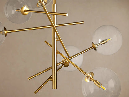 Roscoe Chandelier: modern plated brass fixture with multiple arms radiating out, holding clear glass globes with illuminated bulbs.