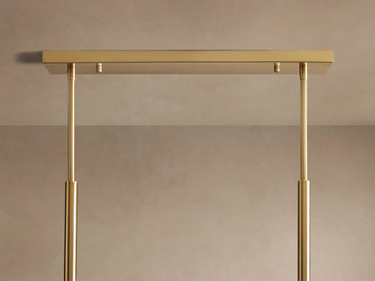Roscoe Linear Chandelier. Close-up of the rectangular golden brass canopy with two sleek support rods against a neutral wall.