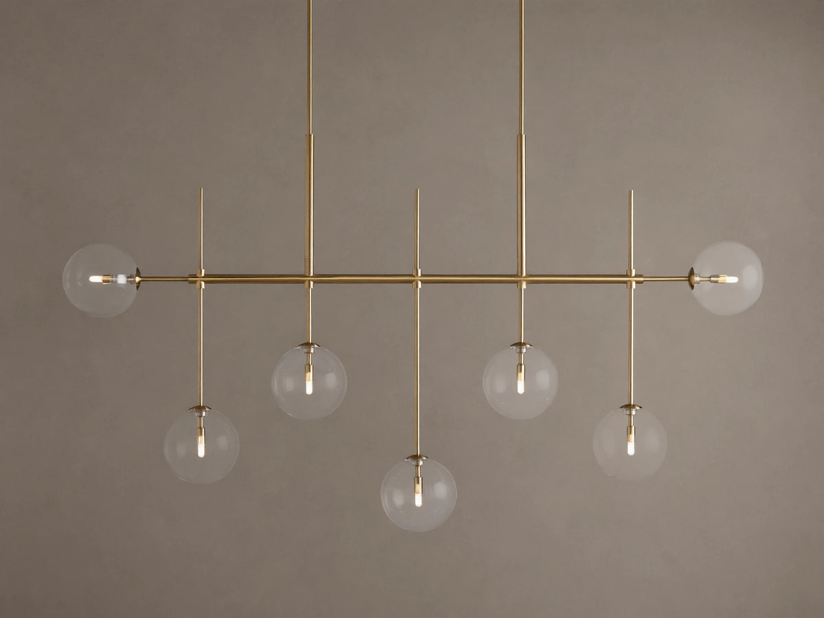 Roscoe Linear Chandelier: 7 illuminated clear glass globe lights on a brass-finished horizontal bar. Angled view.
