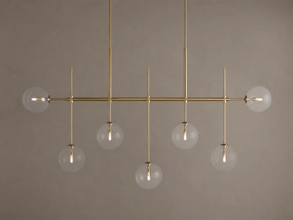 Roscoe Linear Chandelier: 7 illuminated clear glass globe lights on a brass-finished horizontal bar. Angled view.