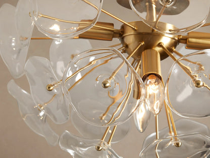 Lily Flush Mount ceiling light with a brass base and clear glass petals, angled view against a beige ceiling.