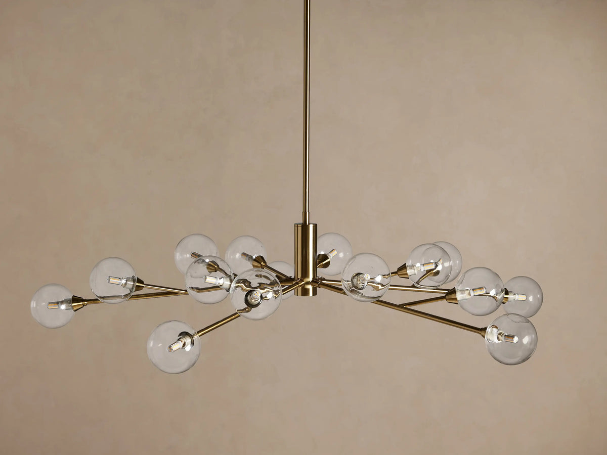 Apollo Round Chandelier in brass finish, featuring radiating arms with clear glass globes, hanging against a warm beige background.