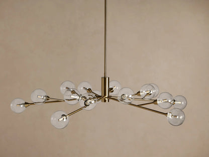 Apollo Round Chandelier in brass finish, featuring radiating arms with clear glass globes, hanging against a warm beige background.