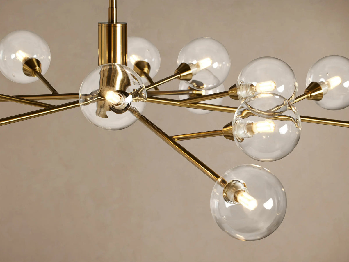 Apollo Round Chandelier, polished brass frame with radiating arms, each holding a clear glass globe, against a beige wall.