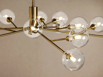 Apollo Round Chandelier, polished brass frame with radiating arms, each holding a clear glass globe, against a beige wall.