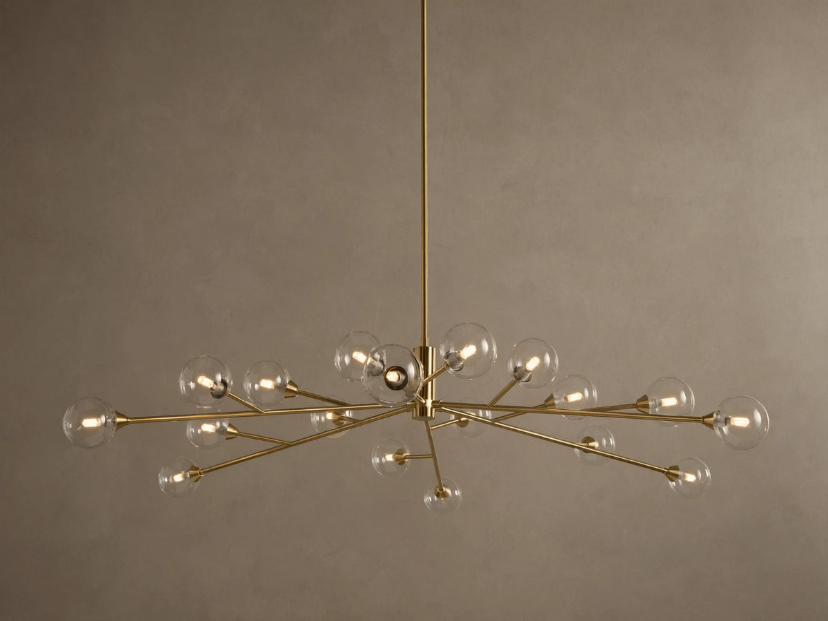 Apollo Round Chandelier: Brass-toned arms with many illuminated clear glass globe bulbs, suspended against a textured wall.