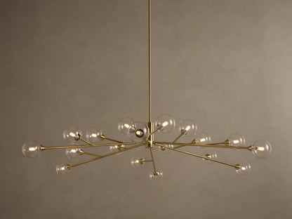 Apollo Round Chandelier: Brass-toned arms with many illuminated clear glass globe bulbs, suspended against a textured wall.