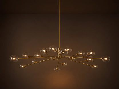 Apollo Round Chandelier: Brass-toned arms with many illuminated clear glass globe bulbs, suspended against a textured wall.