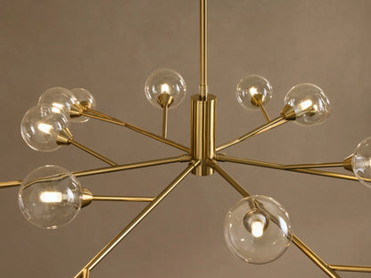 Apollo Round Chandelier: polished gold frame, starburst design, with many clear spherical bulbs against a neutral wall.