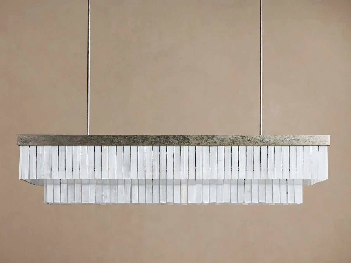 Cameron Rectangular Chandelier with antique silver frame & two tiers of glowing white selenite blades, suspended on a brown wall.