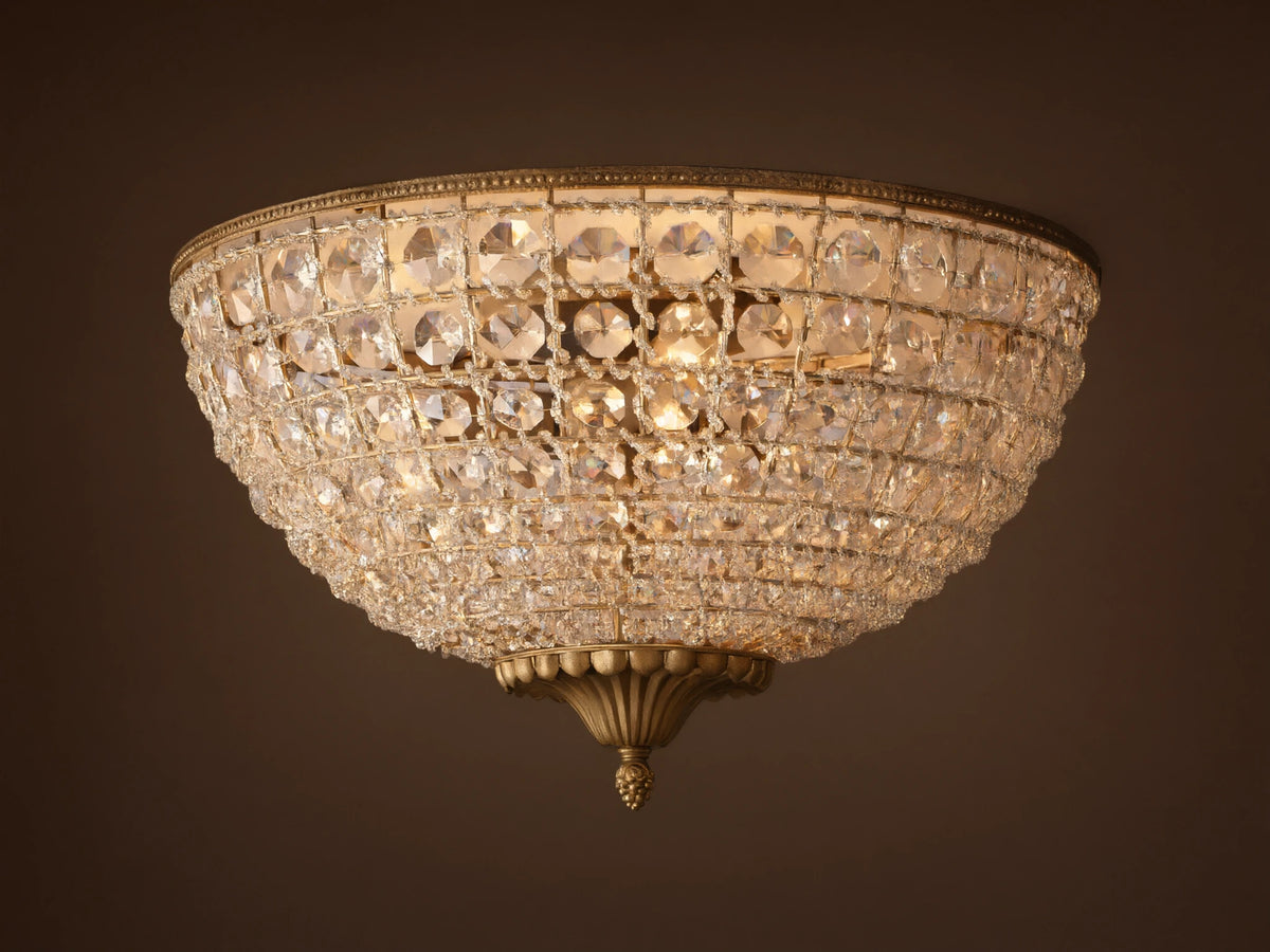 Poppy Flush Mount. Dome-shaped fixture with rows of clear faceted crystals and antique brass accents, glowing warmly on a ceiling.