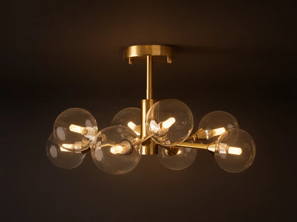 Apollo Flush Mount with 8 illuminated clear globe bulbs on a polished brass frame, mounted flush against a beige ceiling.