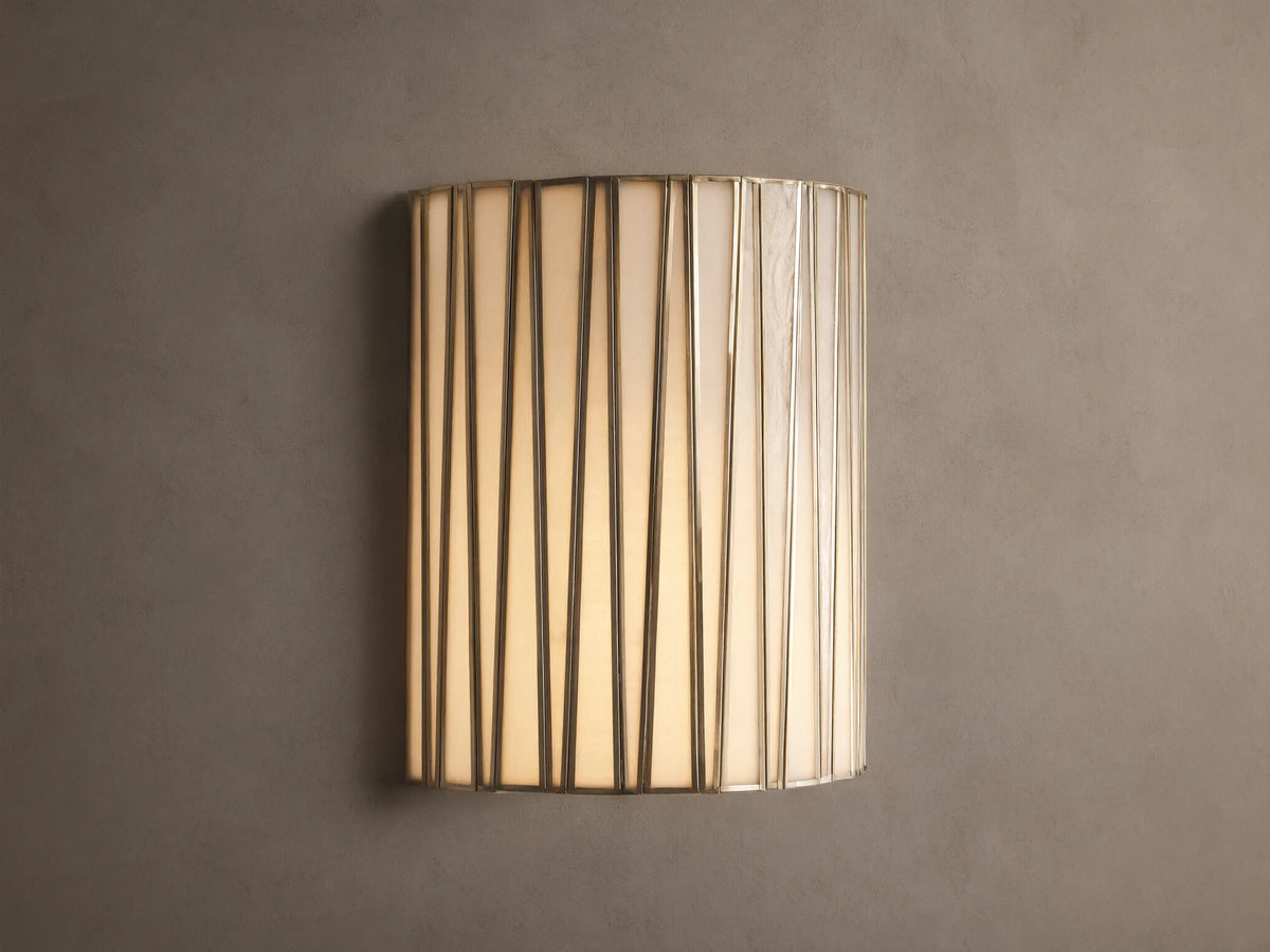 Jeunet Sconce, glowing, with vertical antiqued brass iron strips over translucent white glass, mounted on a neutral wall.