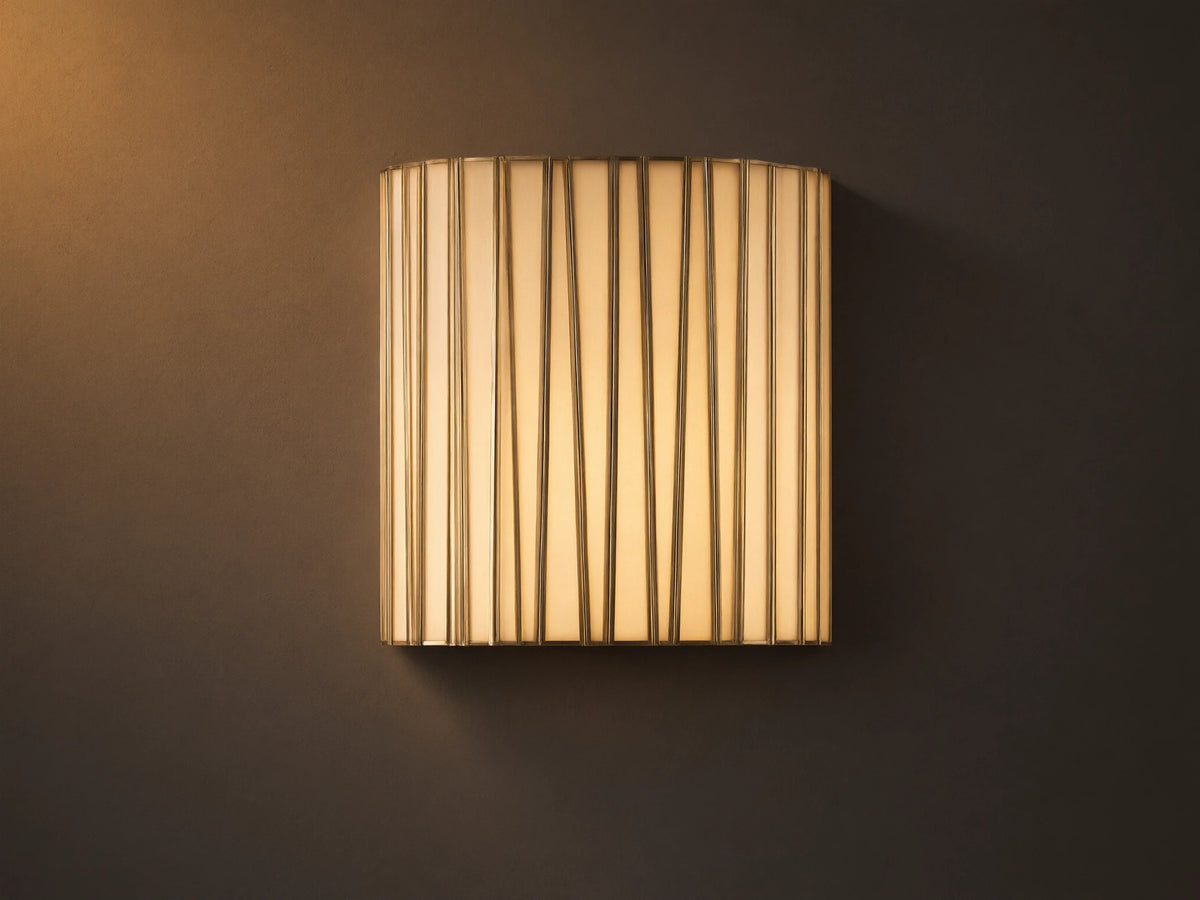 Jeunet Sconce, glowing, with vertical antiqued brass iron strips over translucent white glass, mounted on a neutral wall.
