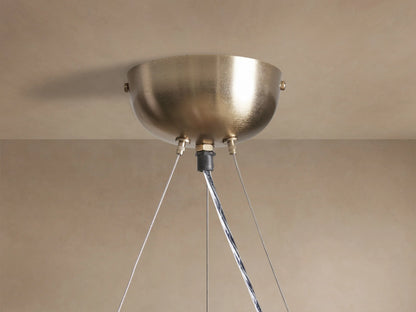 Close-up of a lit Jeunet Round Chandelier with an antiqued brass frame and geometric translucent glass panels, angled view.