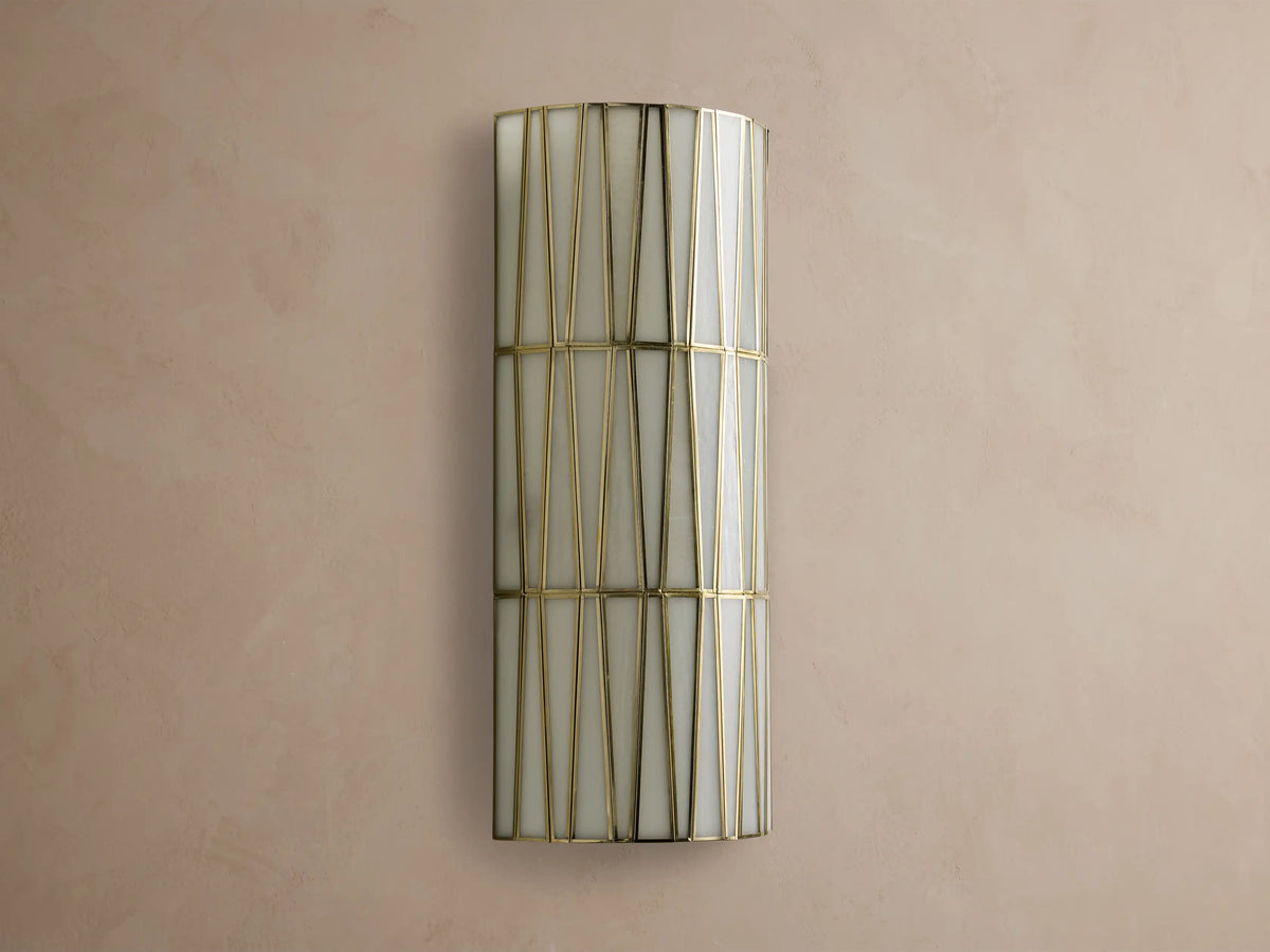 Jeunet Sconce, a rectangular wall-mounted light with an antiqued brass frame creating geometric patterns over illuminated white glass.