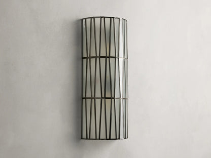 Jeunet Sconce with antiqued brass finish, features two glowing lights behind a cylindrical iron frame with vertical and diagonal lines.