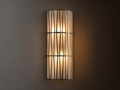 Jeunet Sconce with antiqued brass finish, features two glowing lights behind a cylindrical iron frame with vertical and diagonal lines.