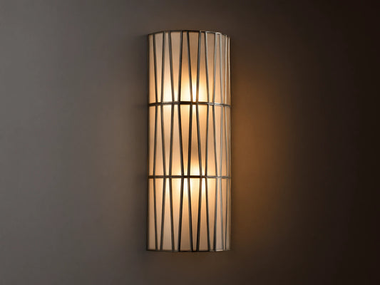 Jeunet Sconce with antiqued brass finish, features two glowing lights behind a cylindrical iron frame with vertical and diagonal lines.