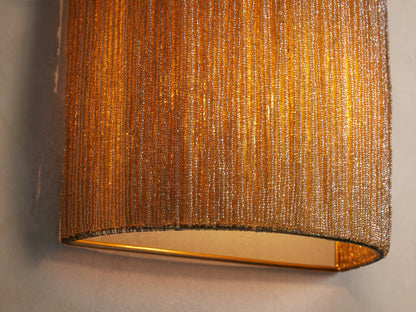 Romilly Beaded Sconce, vertical and curved, covered in dense, shimmering golden-bronze glass beads, mounted on a light wall.