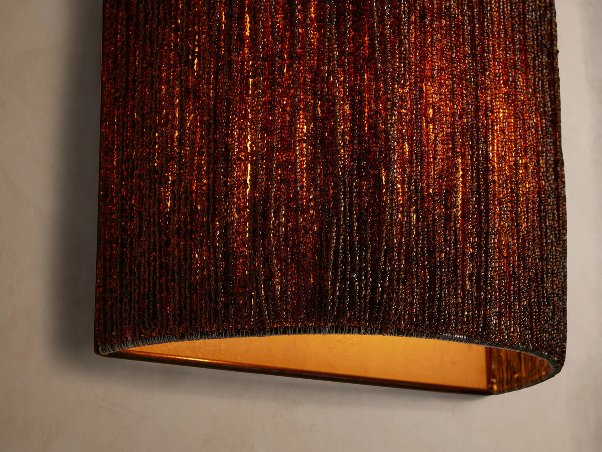 Romilly Beaded Sconce: curved, rectangular, dark brown glass-beaded wall light, mounted vertically on a light wall.