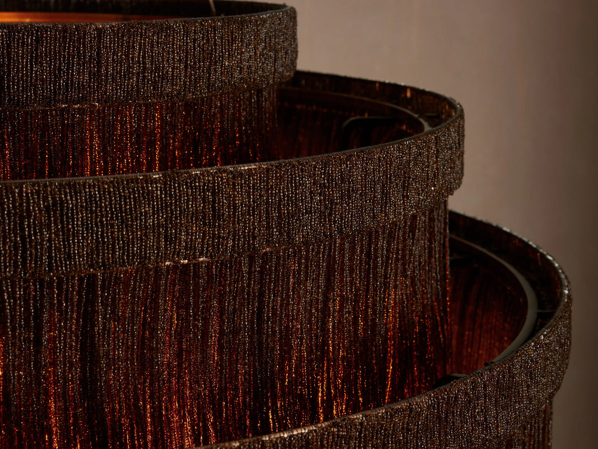 Close-up of Romilly Tiered Chandelier, showing multiple dark tiers of glass beads glowing with warm orange light.