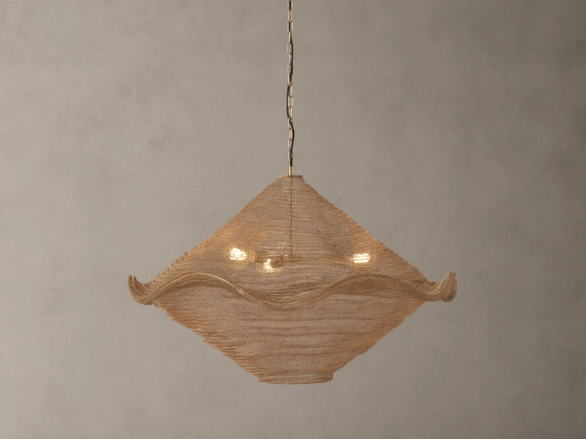 Mirza Sphere Chandelier. Draped woven antique brass mesh in a square shape with wavy edges, 3 glowing bulbs inside, hanging.
