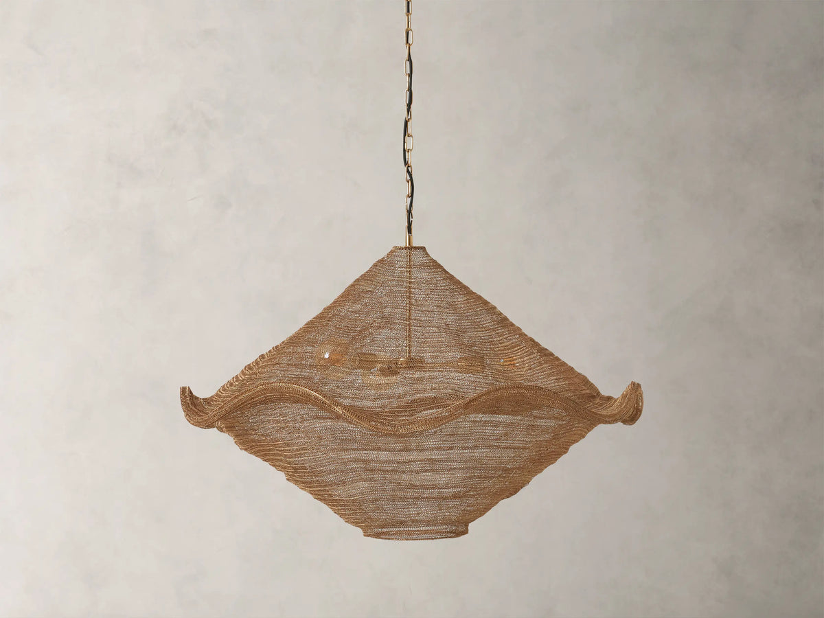 Mirza Sphere Chandelier. Draped woven antique brass mesh in a square shape with wavy edges, 3 glowing bulbs inside, hanging.