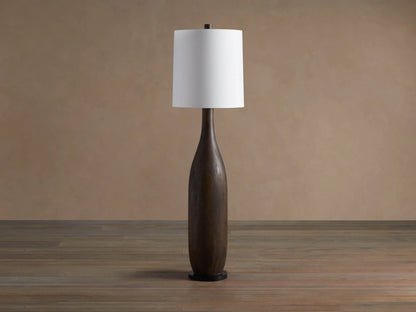 A tall Briar Floor Lamp with a dark espresso, slender wooden base and a glowing white linen cylinder shade on a wooden floor.