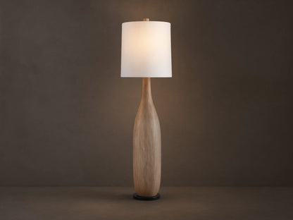 Briar Floor Lamp: natural wood, bottle-shaped base, with a white cylindrical linen shade, standing upright on a wood floor.