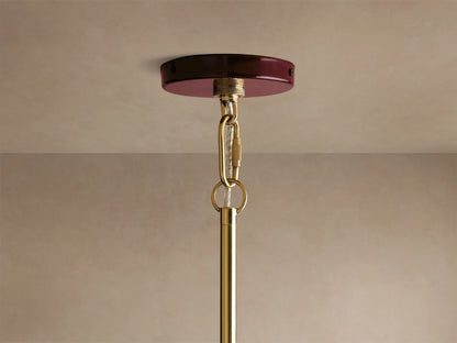 Shiny burgundy and gold pendant light with a glossy finish, showcasing warm glowing bulbs, creating an inviting ambiance in a cozy setting.