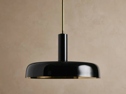 Bonham Pendant: sleek black metal domed shade with a gleaming brass interior, suspended from a brass rod against a textured beige wall.