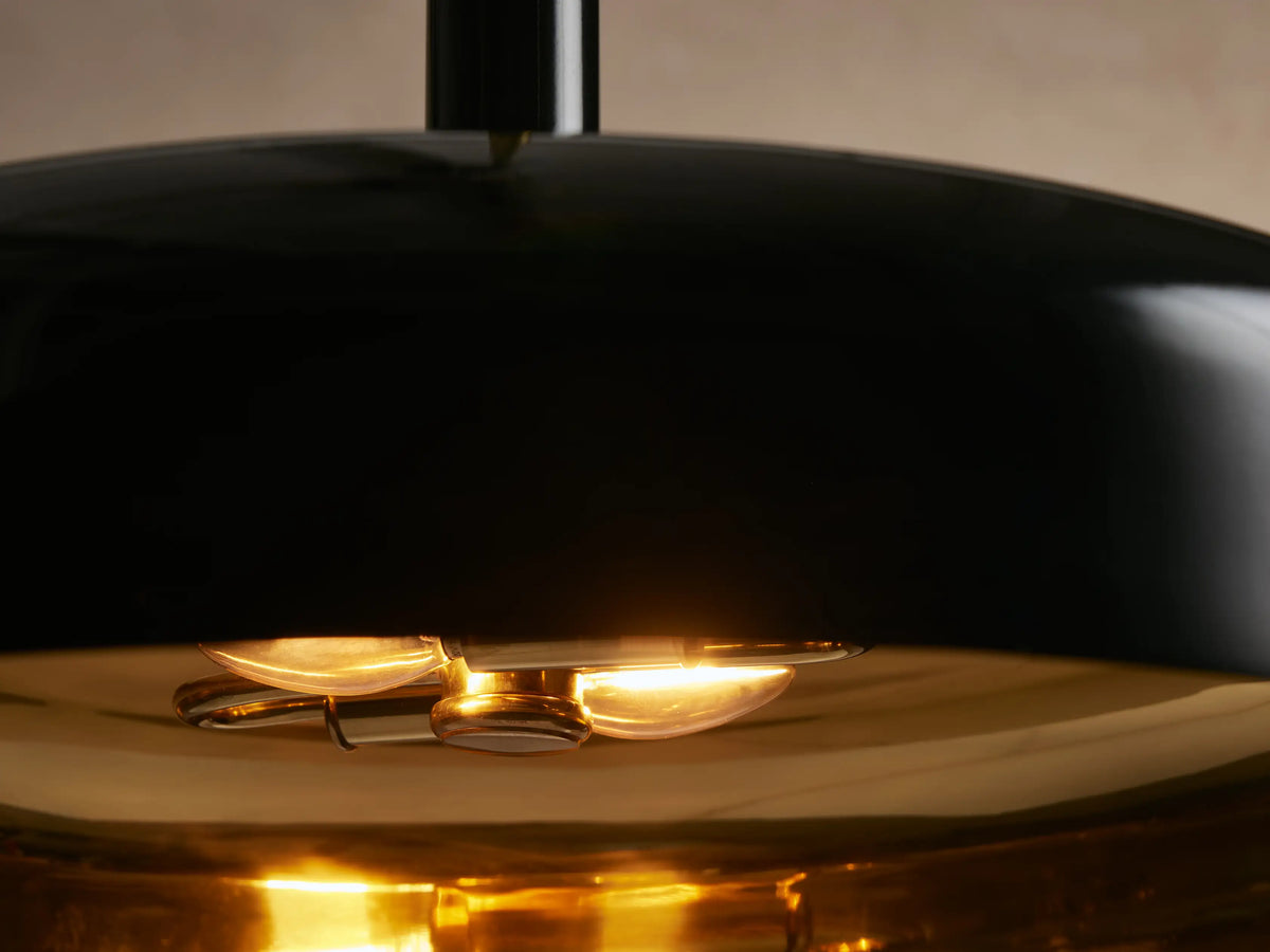 Bonham Pendant: black bell-shaped shade with a contrasting brass interior, hanging from a brass rod against a neutral wall.