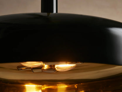 Bonham Pendant: black bell-shaped shade with a contrasting brass interior, hanging from a brass rod against a neutral wall.