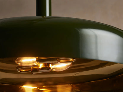 Bonham Pendant, dark green powder-coated dome shade with brass interior, suspended from a brass rod against a light wall.