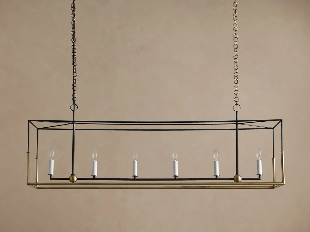 Holt Linear Chandelier. Black rectangular frame with antique brass base, hanging from chains. Six illuminated candle-style bulbs.