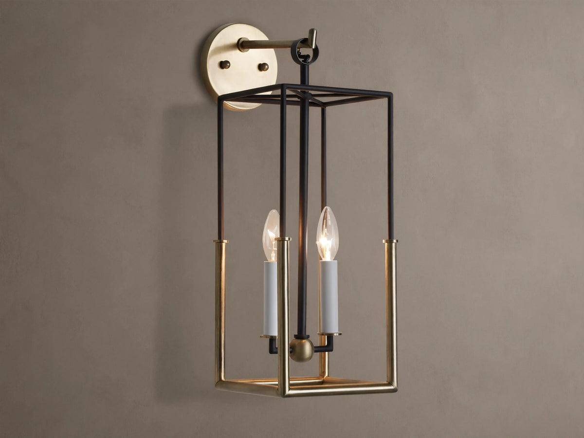 Holt Sconce: rectangular lantern-style light with black iron and antiqued brass frame, two lit candle-style bulbs on neutral wall.