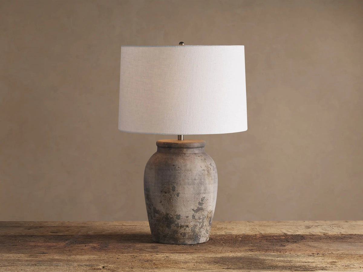 Thornton Table Lamp with distressed dark grey terracotta base, light linen drum shade, on a rustic wooden table.