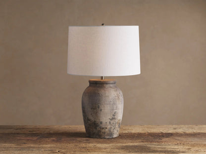 Thornton Table Lamp with distressed dark grey terracotta base, light linen drum shade, on a rustic wooden table.