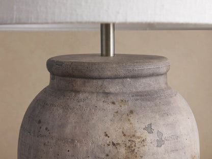 Thornton Table Lamp. Distressed dark grey terracotta base, white linen shade on a rustic wooden table.